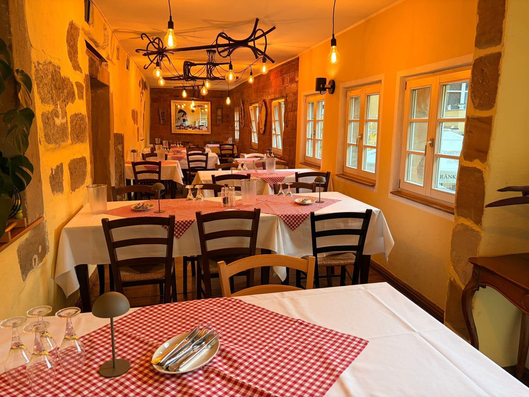 Gastraum der Trattoria Amici mit gedeckten Tischen, Natursteinwand und warmem Abendlicht